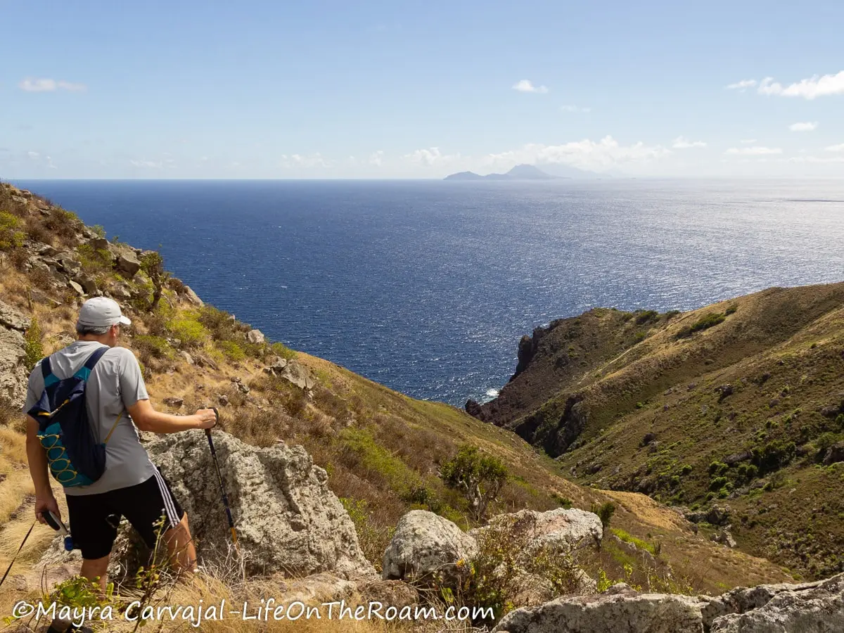 A man on a trail overlooking two grassy hills and an island in the far distance