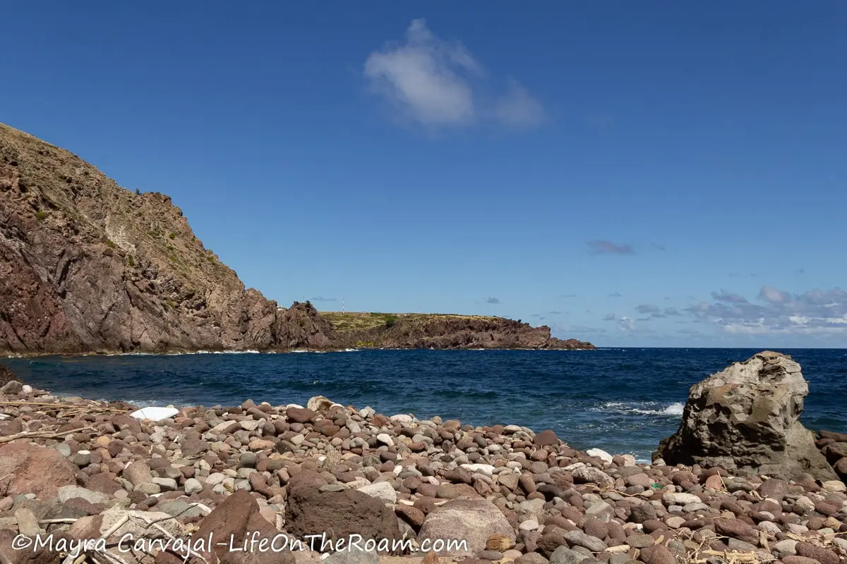 A beach with big boulders and a hill in the background
